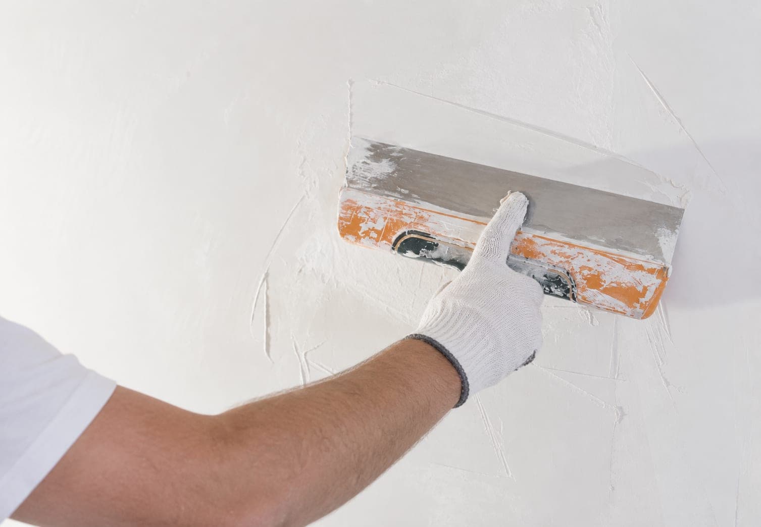 Nahaufnahme einer Hand, die eine Wand mit der Glättkelle glatt spachtelt