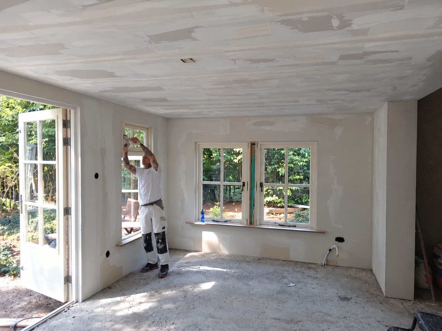 Stukadoor aan het werk bij het raam in de tuinkamer, tuindeuren open
