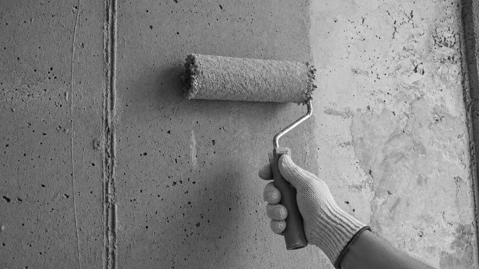 Hand with a roller applying primer to a concrete wall